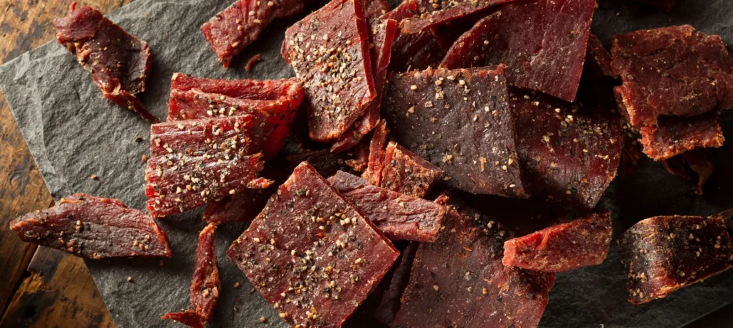 Beef Jerky is a meat snack that has been marinated in spices, sliced into thin strips and dried or smoked. It has its origins in South America where indigenous people dried meat as a way to preserve it.